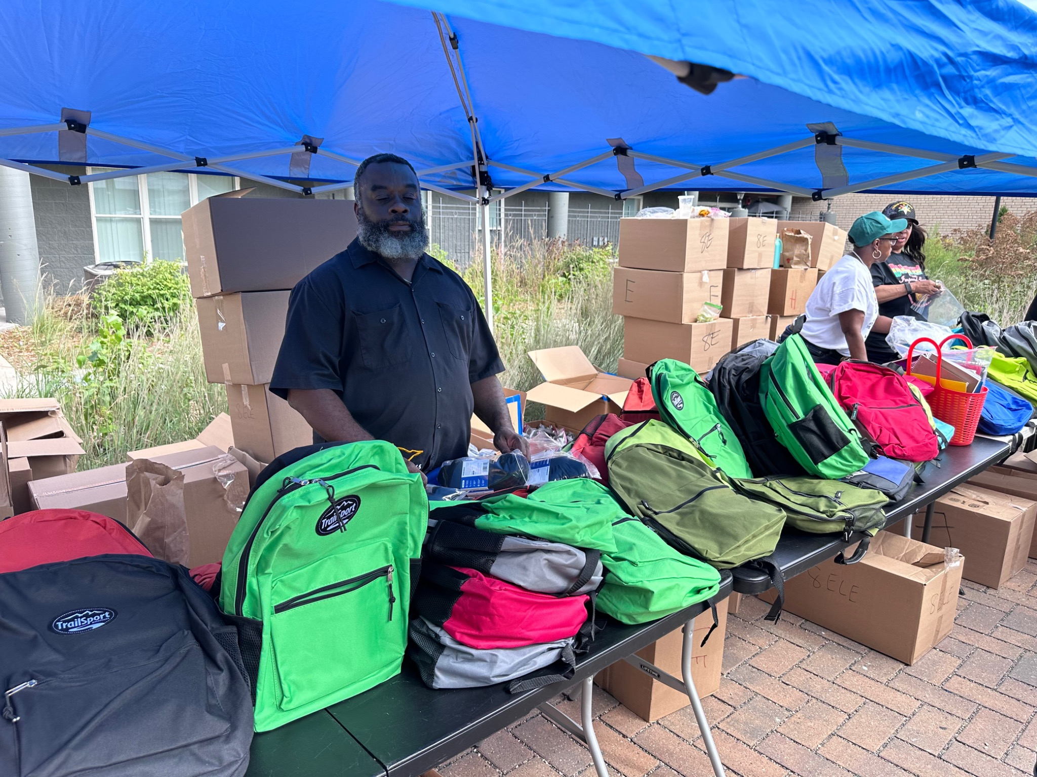 Volunteers distributing backpacks under a blue tent at the Fresh and Fly Bash